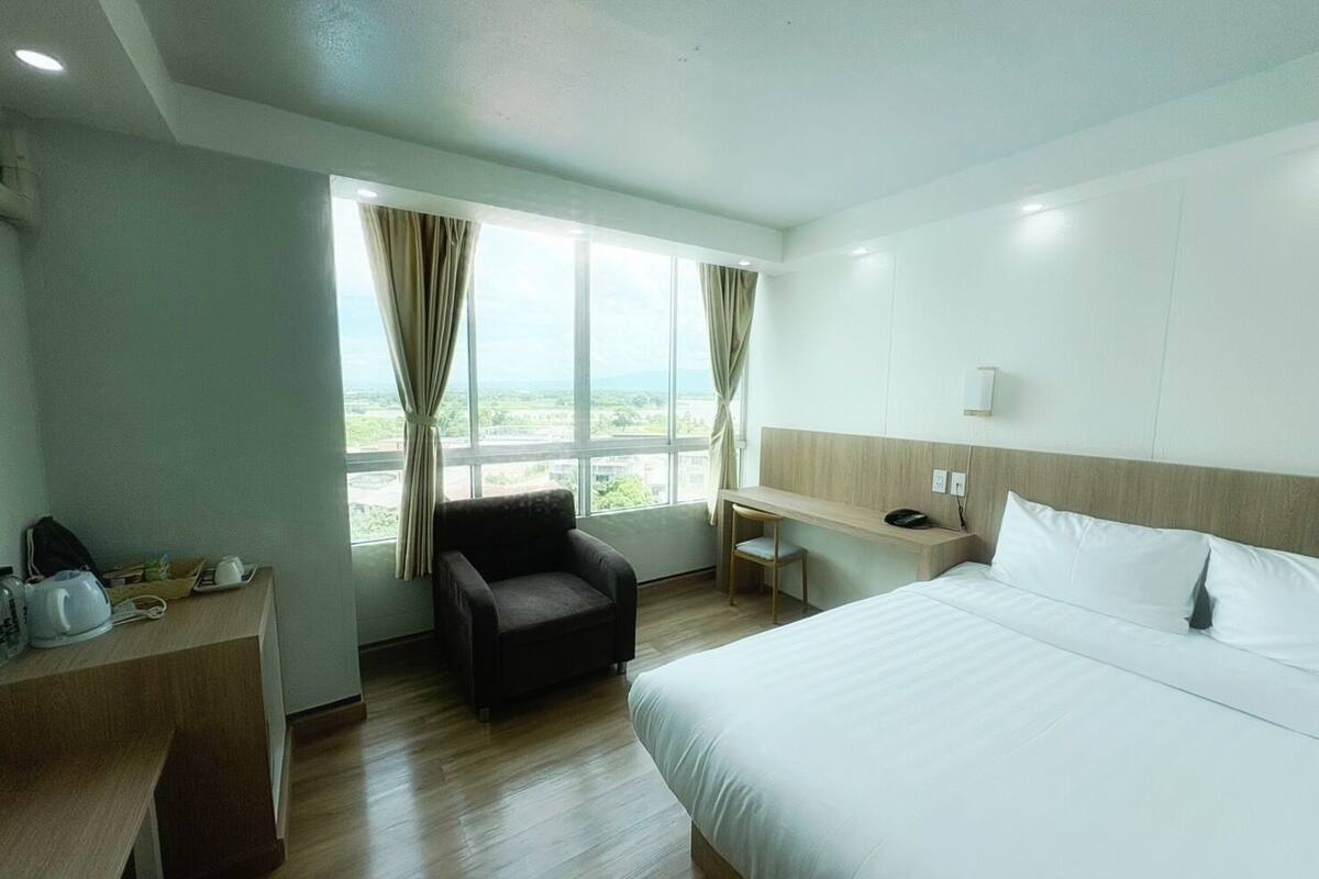 A hotel room with a bed, a desk, a chair, and a view of the outdoors.