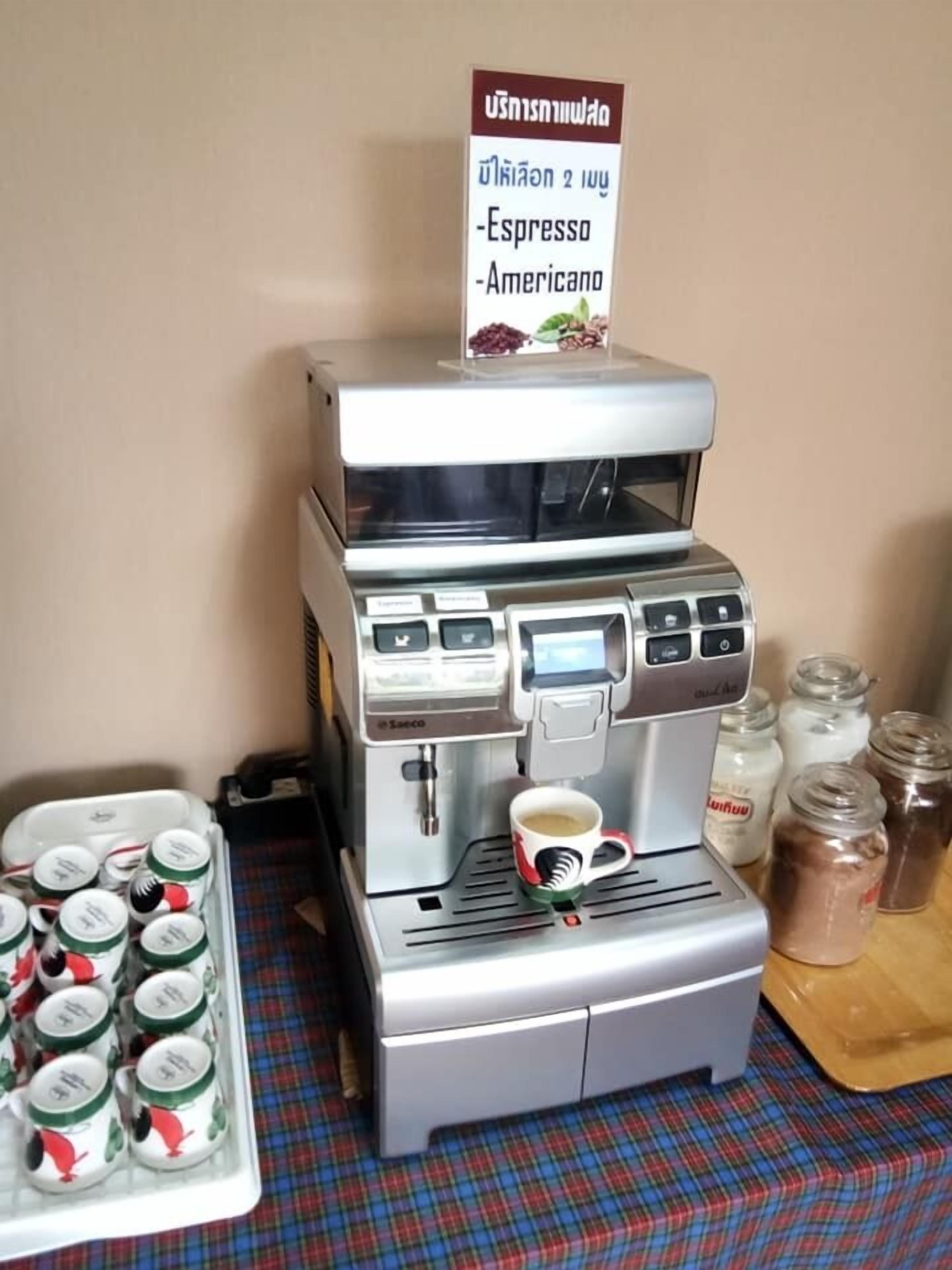 Máquina de café com um letreiro com o menu acima, uma chávena de café sobre a máquina e uma bandeja com cápsulas de café à esquerda.