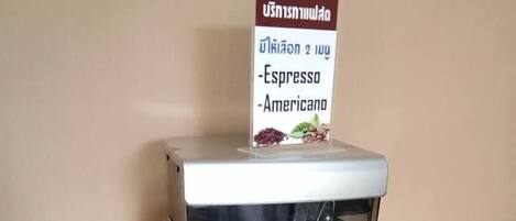 Máquina de café com um letreiro com o menu acima, uma chávena de café sobre a máquina e uma bandeja com cápsulas de café à esquerda.