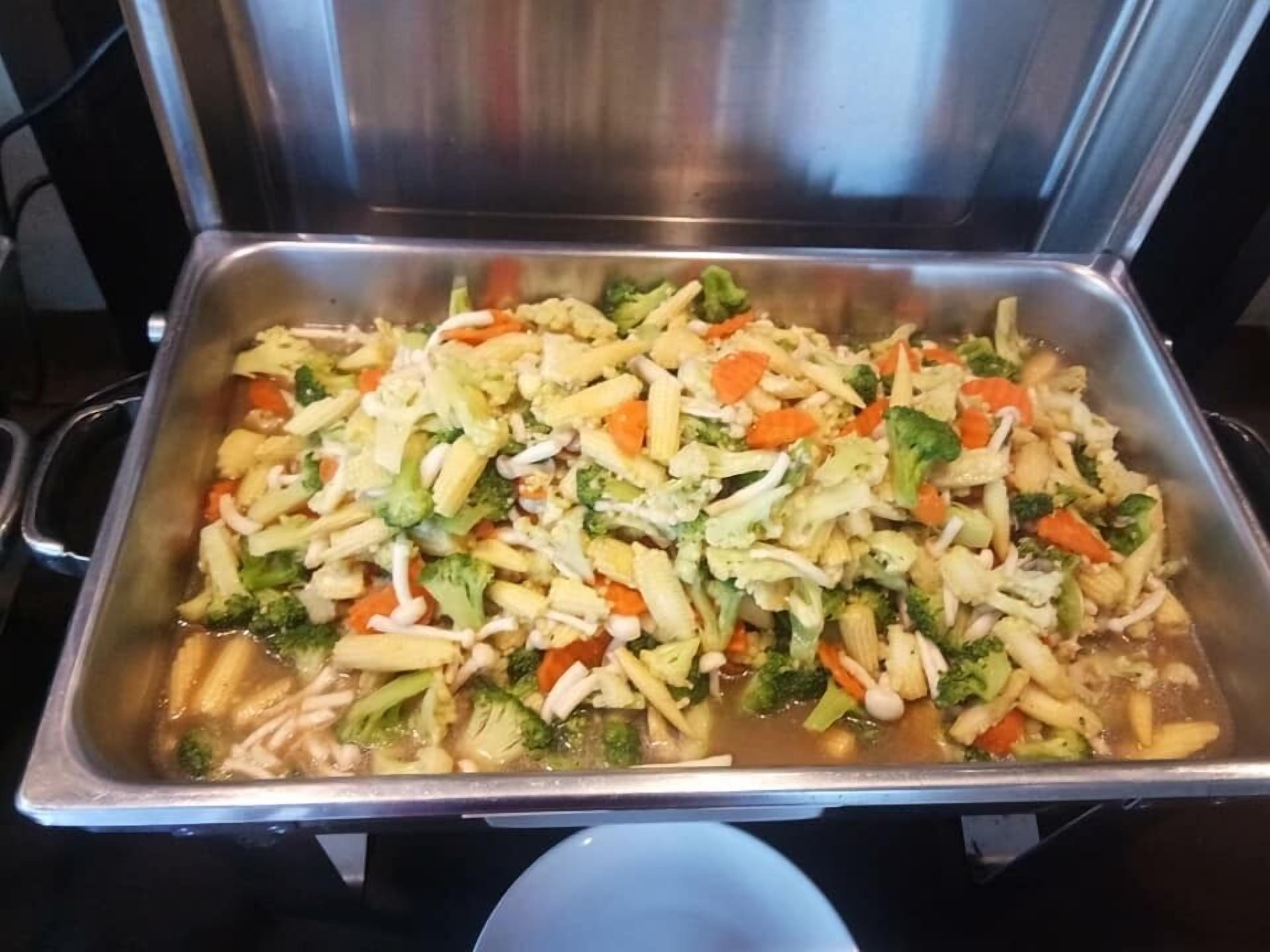 A stainless steel buffet tray filled with a variety of vegetables and pasta.