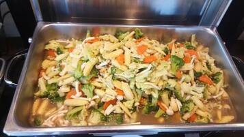 A stainless steel buffet tray filled with a variety of vegetables and pasta.