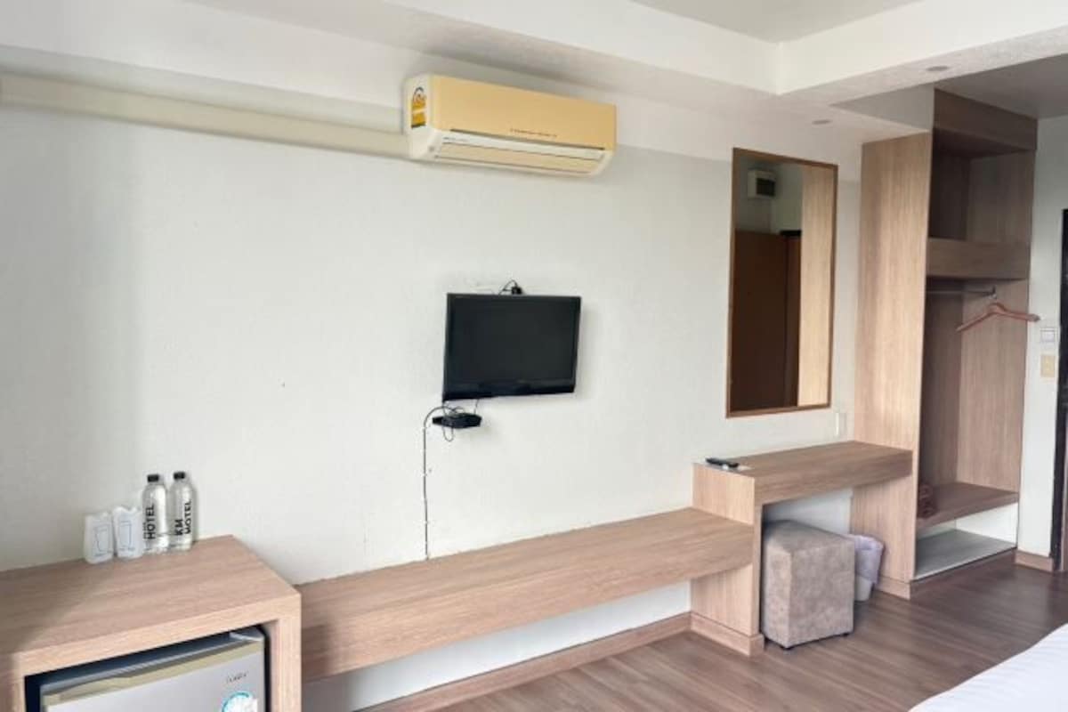 Una habitación de hotel moderna con un televisor de pantalla plana en la pared, un banco de madera, un pequeño otomaní y un armario empotrado.
