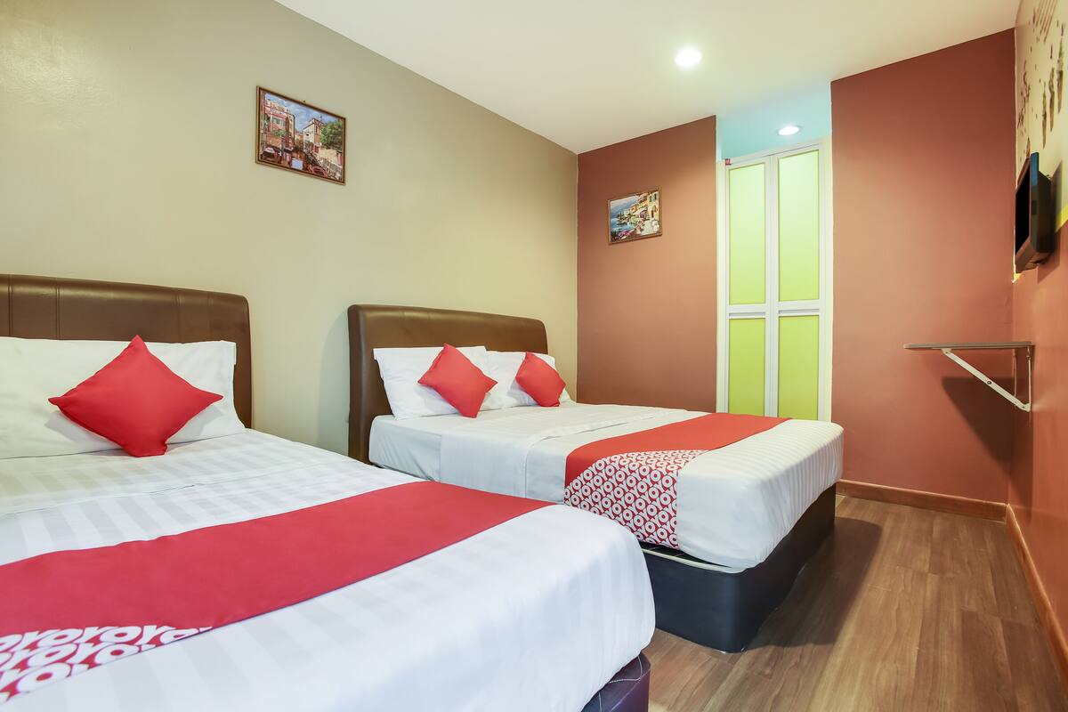 Ein Hotelzimmer mit zwei Betten, jeweils mit rot-weiß gestreifter Bettwäsche, und einem kleinen Fenster mit Blick auf Grün.
