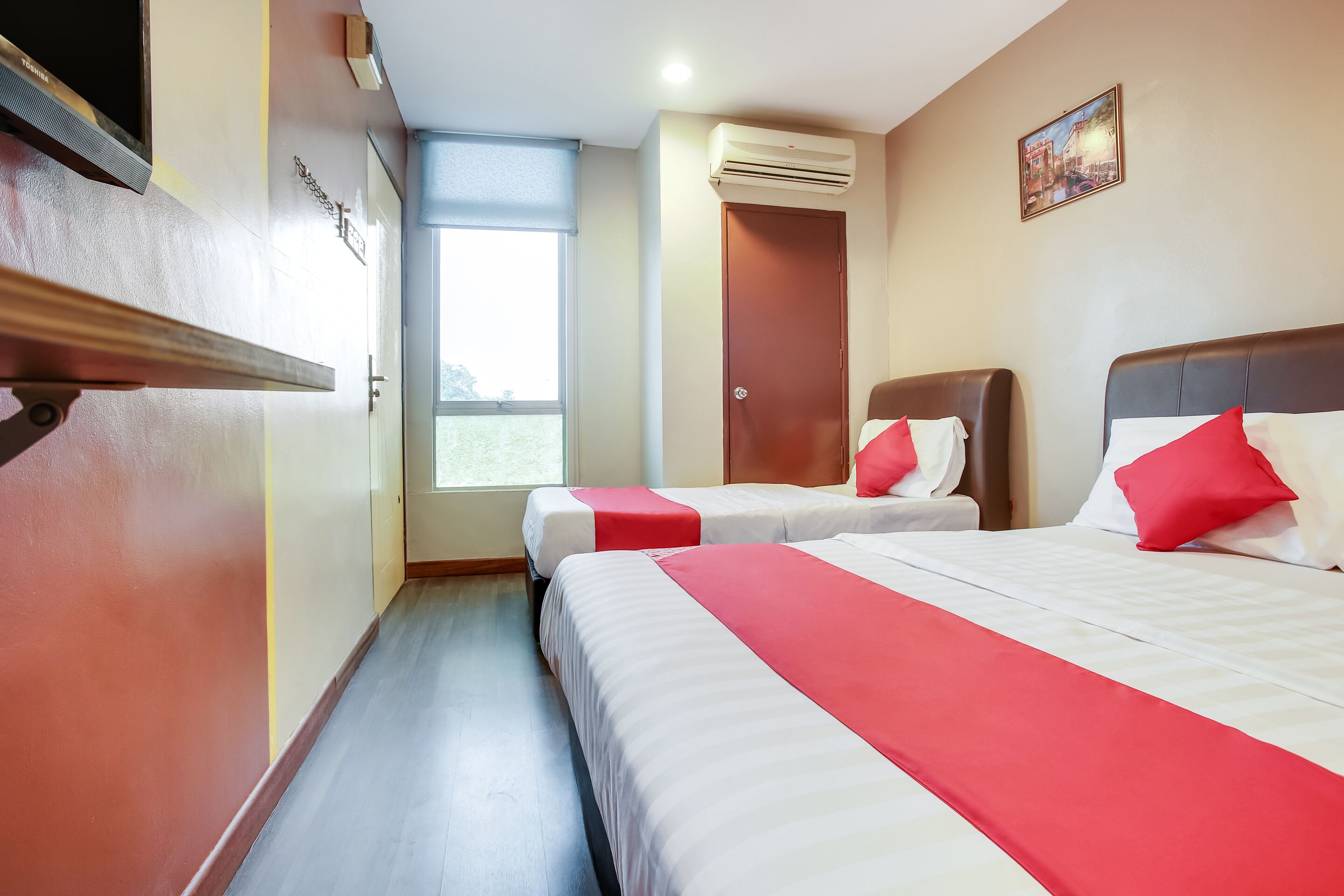 A hotel room with two beds, a TV, an air conditioner, and a window with a view.