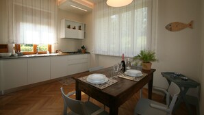 A modern kitchen with white cabinets, a wooden dining table set with plates and glasses, and a fish-shaped wall decoration.
