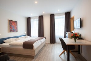 Habitación de hotel moderna con cama, escritorio, silla, televisor y un cuadro en la pared.