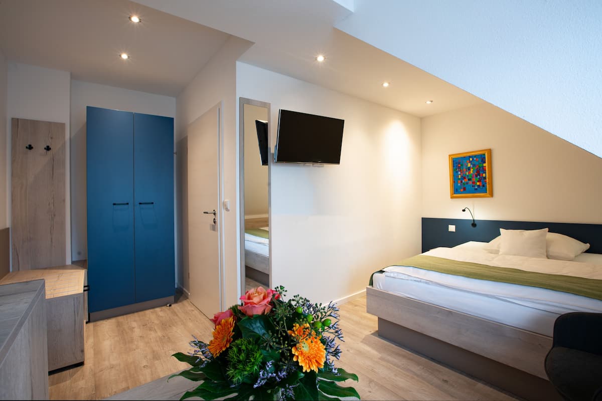 A bedroom with a bed, a TV mounted on the wall, a blue wardrobe, and a floral arrangement.