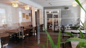 A restaurant with wooden tables and chairs, a glass partition, and a view of the street. - Caesaro Hotel & Pizzeria (Hagen am Teuteburger Wald)