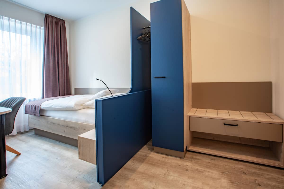 A modern hotel room with a bed, a desk, and a built-in wardrobe.