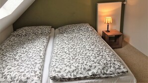 Een slaapkamer met twee bedden, een nachtkastje met een lamp en een raam met gordijnen.