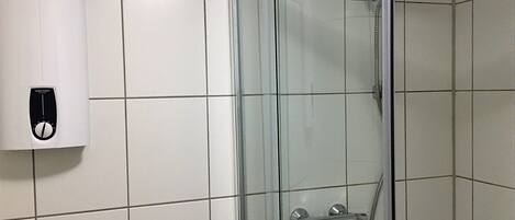 Ducha con mampara de vidrio, cabezal de ducha de mano y panel de control en la pared.