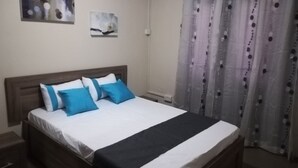 A neatly made bed with blue and white bedding, a wooden headboard, and a grey curtain with a dotted pattern. - Modern and cozy apartment (Pereybere)