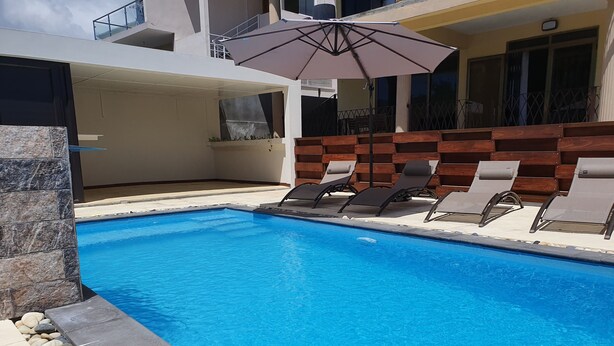 A swimming pool with lounge chairs and an umbrella. - Modern and cozy apartment (Pereybere)