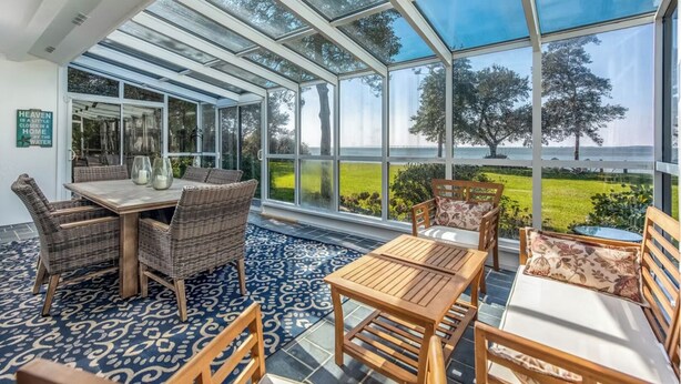 Un solarium con un amplio ventanal, muebles de mimbre y vistas a un paisaje verde.
