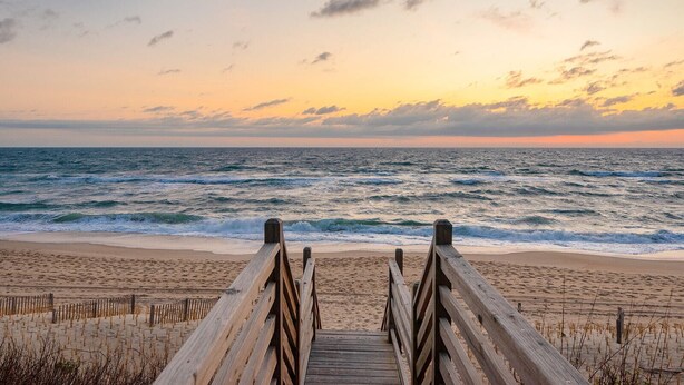 Una passerella di legno che conduce a una spiaggia, con onde e un tramonto sullo sfondo.