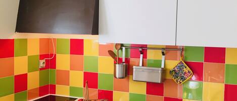 Una cocina con un colorido salpicadero de azulejos, una estufa a gas, un fregadero y un refrigerador.