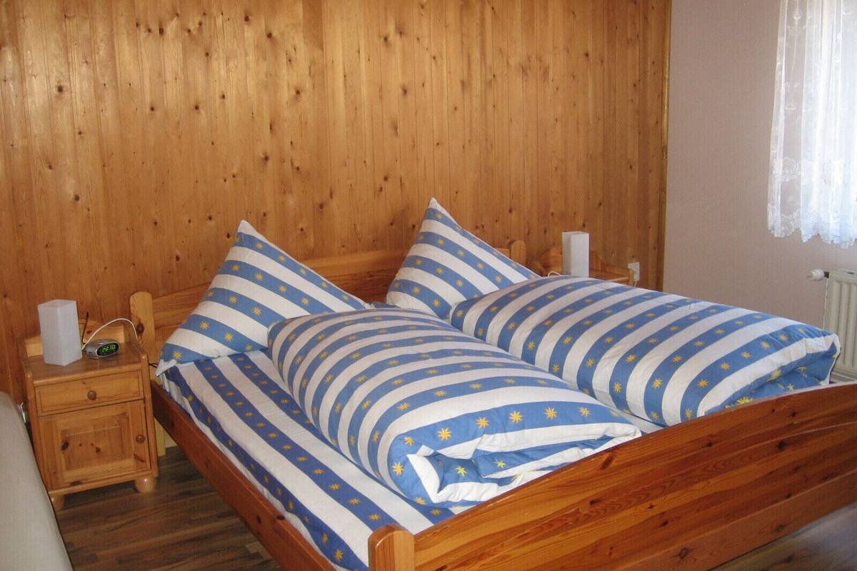 A wooden bed with striped bedding in a room with wooden walls and a nightstand.
