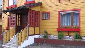 A yellow building with red trim, a wooden staircase, and a brick foundation. - Ferienwohnungen an der Loipe (Braunlage)
