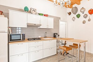 A modern kitchen with white cabinets, a microwave, a gas stove, and a wooden table with two chairs. - GuestHost - Norman Palace Stylish Apartment (Palermo)