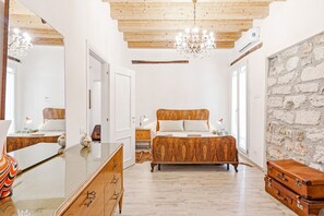 A bedroom with a wooden bed, a dresser, a mirror, and a stone wall. - GuestHost - Norman Palace Stylish Apartment (Palermo)