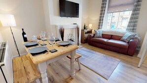 Une chambre meublée comprenant une table à manger dressée pour quatre personnes, un canapé, un téléviseur fixé au mur et une fenêtre avec des rideaux.