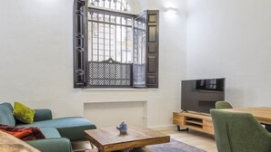 Een woonkamer met een bank, een salontafel, een televisie en een raam met een metalen traliewerk.