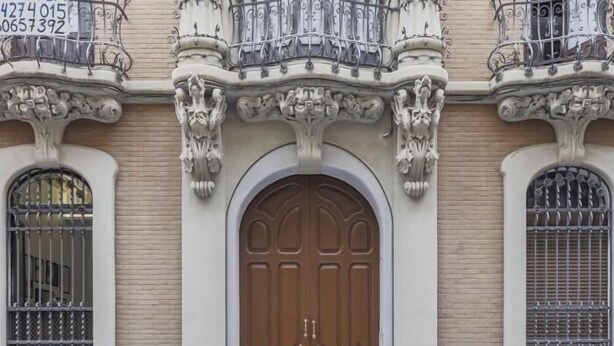 Een gevel met versierde architectonische details, waaronder een grote, rondboogvormige toegang deur en decoratieve ijzerwerk boven de ramen.