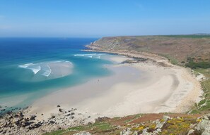 A coastal landscape with a sandy beach, clear blue waters, and rocky cliffs.