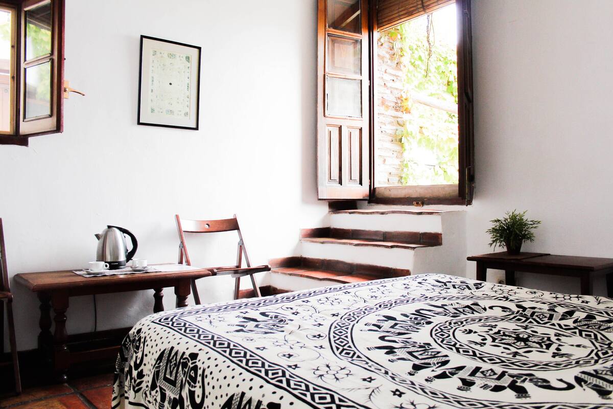 A room with a bed, a desk, a chair, a staircase, and a window.
