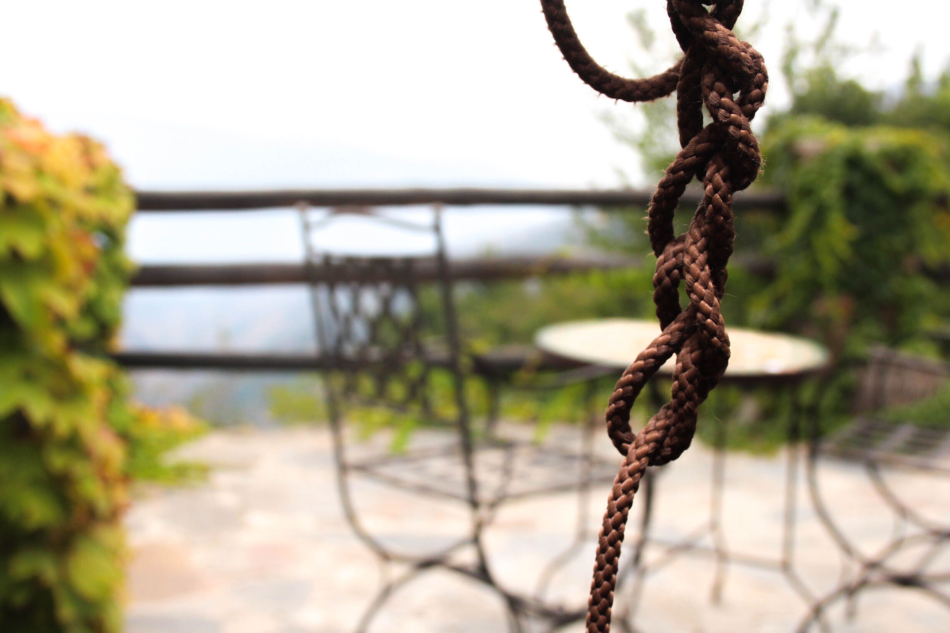 A close-up of a rusty chain against a blurred outdoor background with a table and greenery.