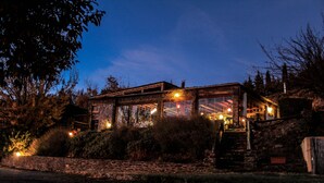 A rustic cabin with a stone foundation, large windows, and a wooden deck. - Casa Rural Catifalarga Capileira (Capileira)