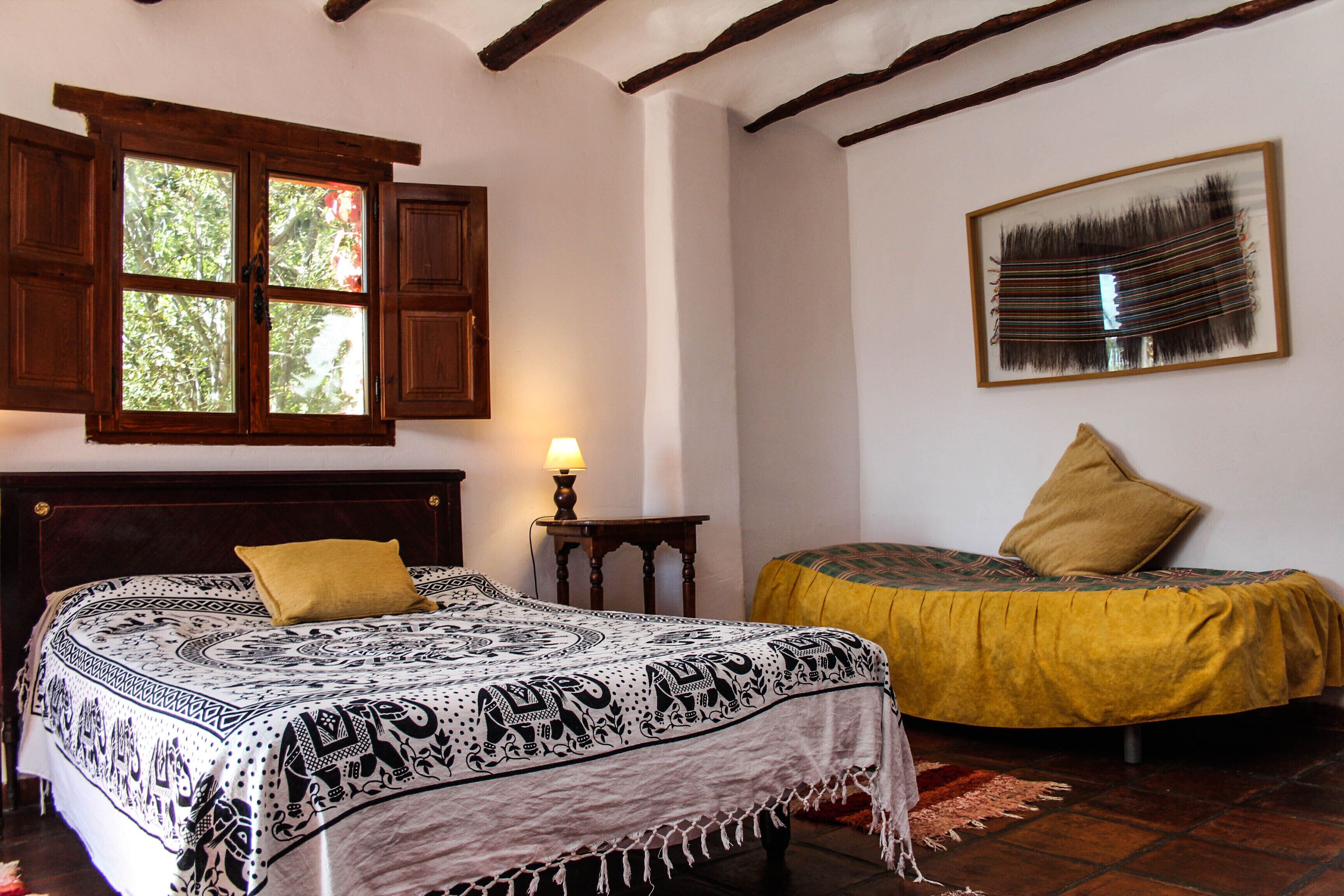A bedroom with a bed, a window, a lamp, a painting, and a chair.