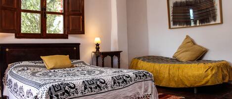 A bedroom with a bed, a window, a lamp, a painting, and a chair.