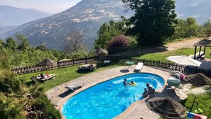 A swimming pool with a stone border, surrounded by lounge chairs and umbrellas, set against a mountainous backdrop. - Casa Rural Catifalarga Capileira (Capileira)