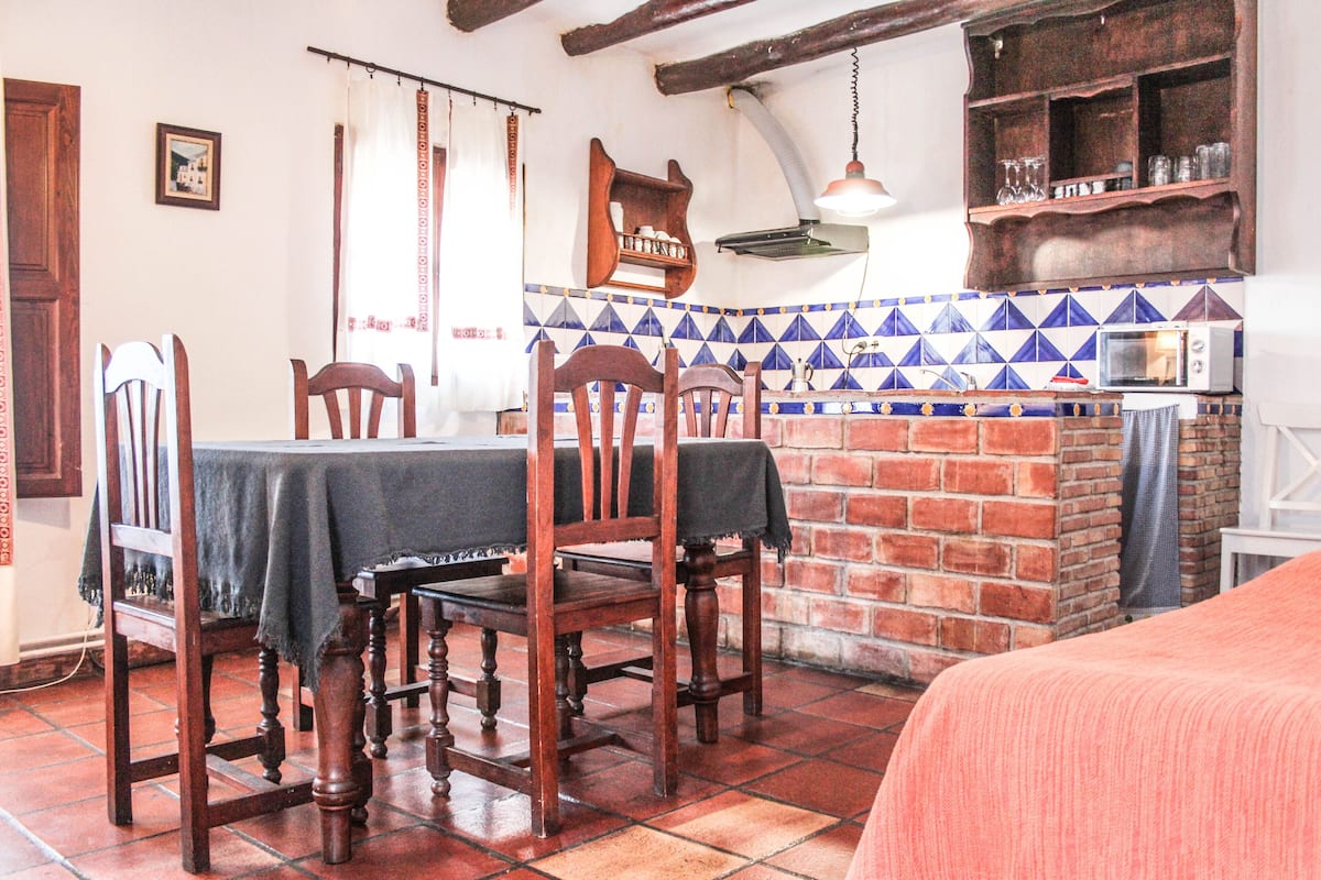 A dining area with a brick wall, tiled backsplash, and a wooden table with chairs.