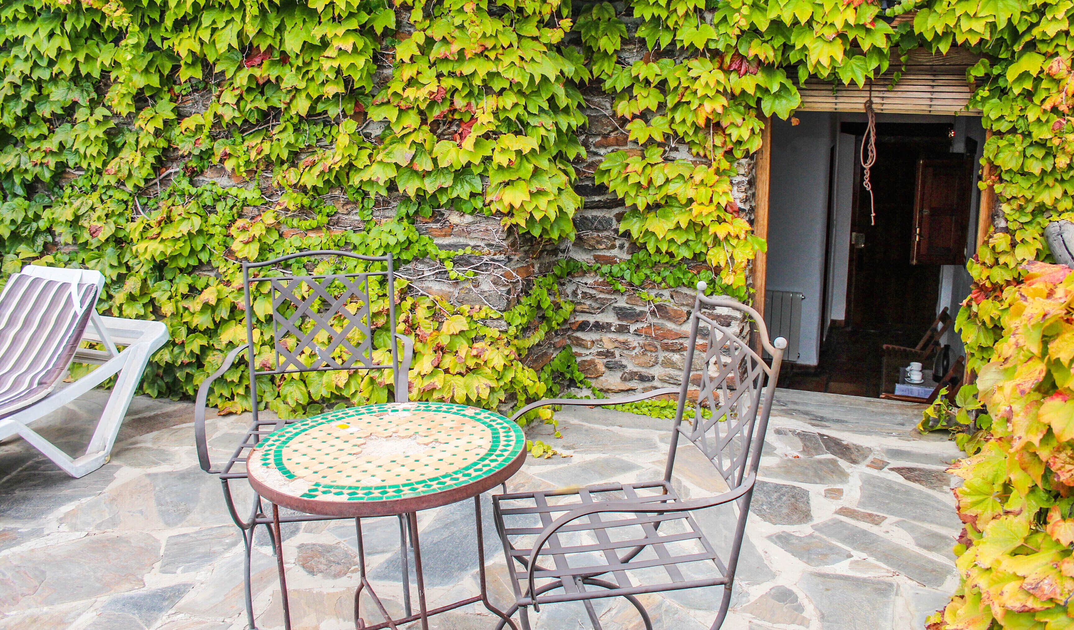 An outdoor patio with a stone floor, two metal chairs, and a table with a green and white mosaic top.