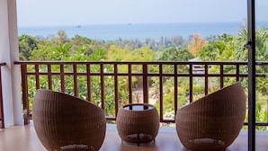 Een balkon met rieten stoelen en een klein tafeltje, met uitzicht op een weelderige tuin en de zee.