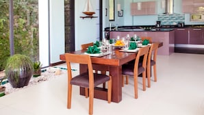 Een eetgedeelte met een houten tafel voor vier personen, omringd door stoelen. Achtergrond toont een keuken met moderne apparatuur.