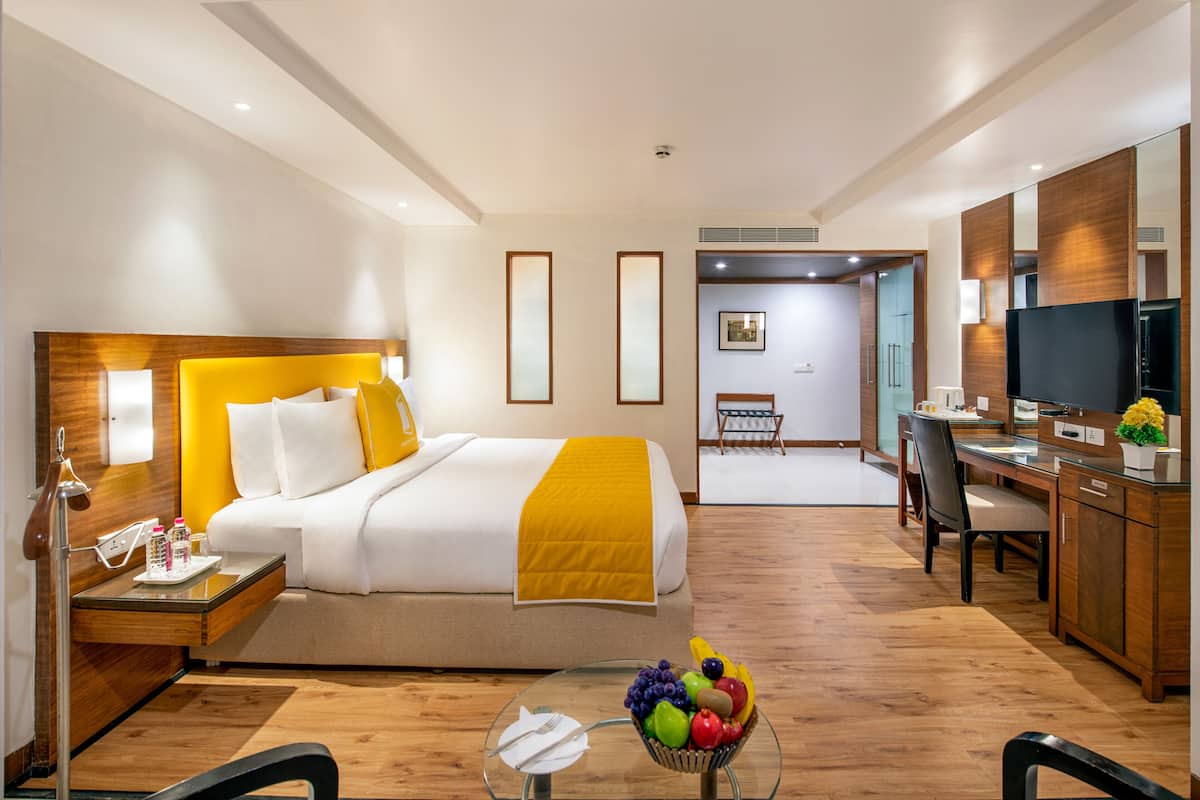 A hotel room with a bed, bedside table, and a fruit bowl on a glass table.