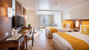 A hotel room with two beds, a desk with a coffee maker, a TV, and a window with curtains. - BloomSuites | Ahmedabad (Ahmedabad)