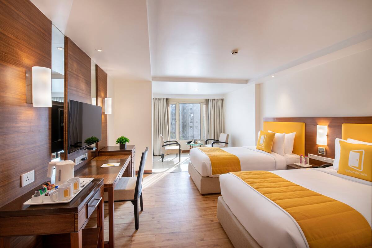 A hotel room with two beds, a desk with a coffee maker, a TV, and a window with curtains.