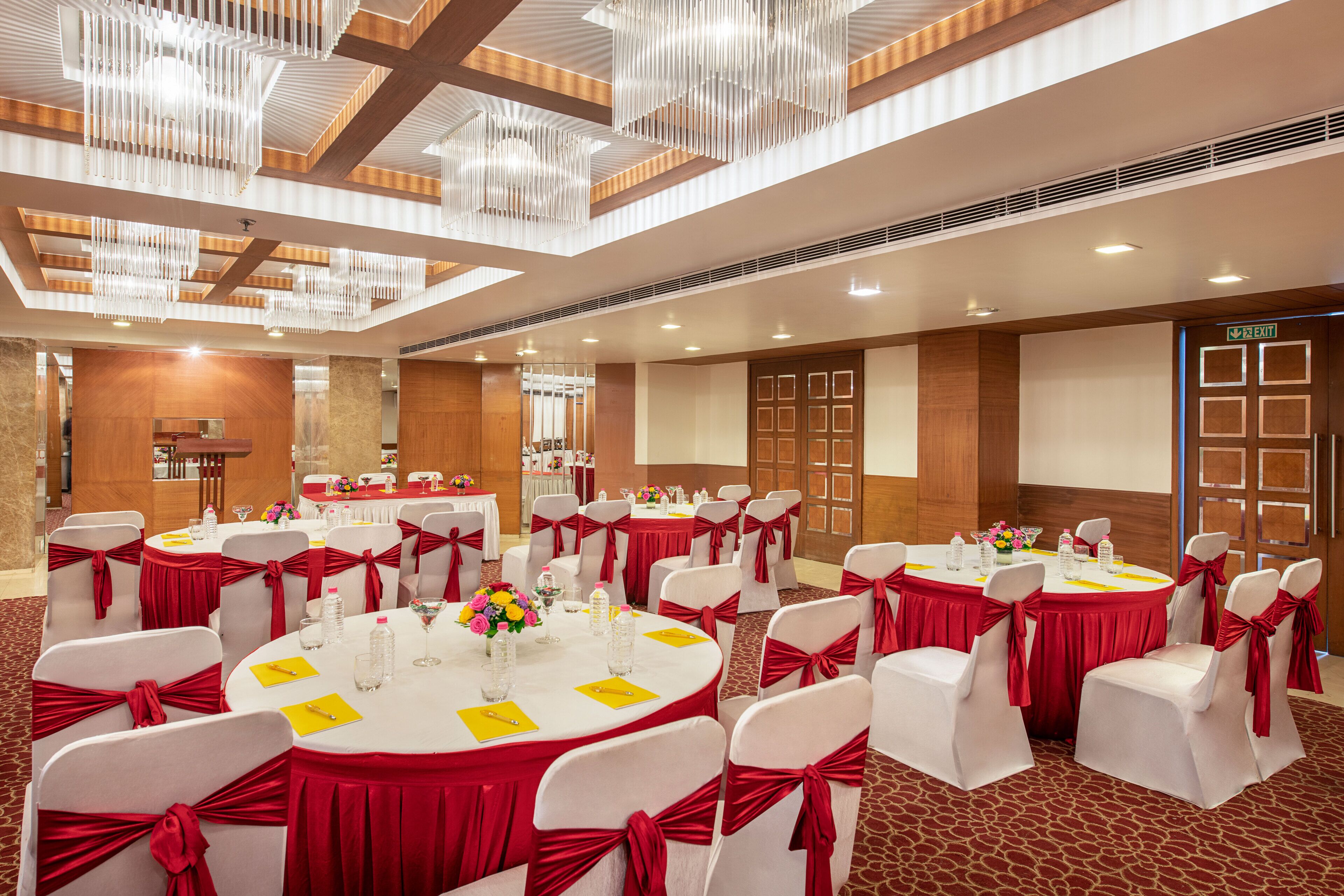 Une salle de banquet avec des tables rondes, des chaises blanches et des rubans rouges.