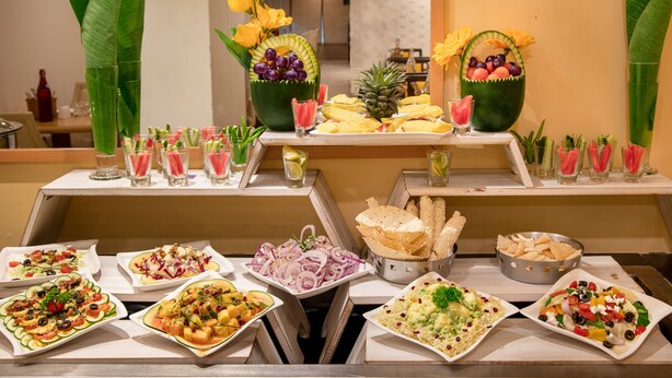 A buffet with various dishes and drinks, including salads, fruits, and bread. - BloomSuites | Ahmedabad (Ahmedabad)