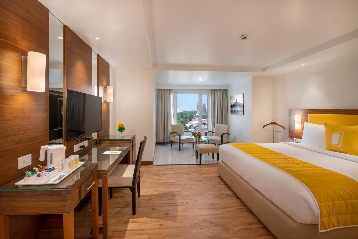 A hotel room with a bed, a desk with a TV, a chair, a sofa, and a dining table.
