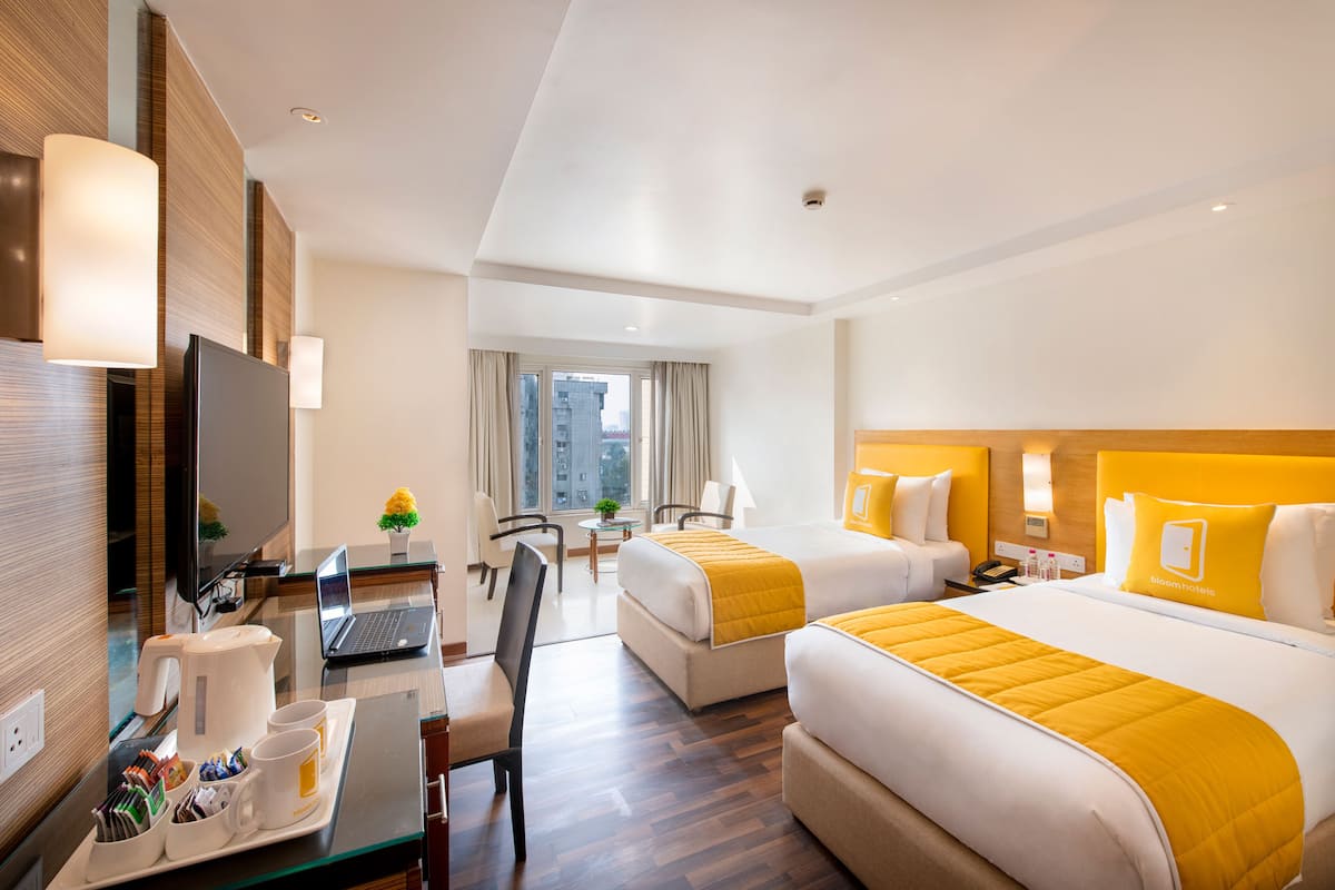 A hotel room with a desk, laptop, two beds, a TV, and a view of the city.