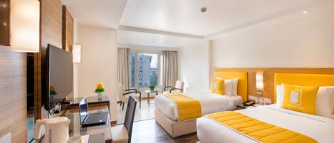 Habitación de hotel con escritorio, computadora portátil, dos camas, televisor y vista a la ciudad.