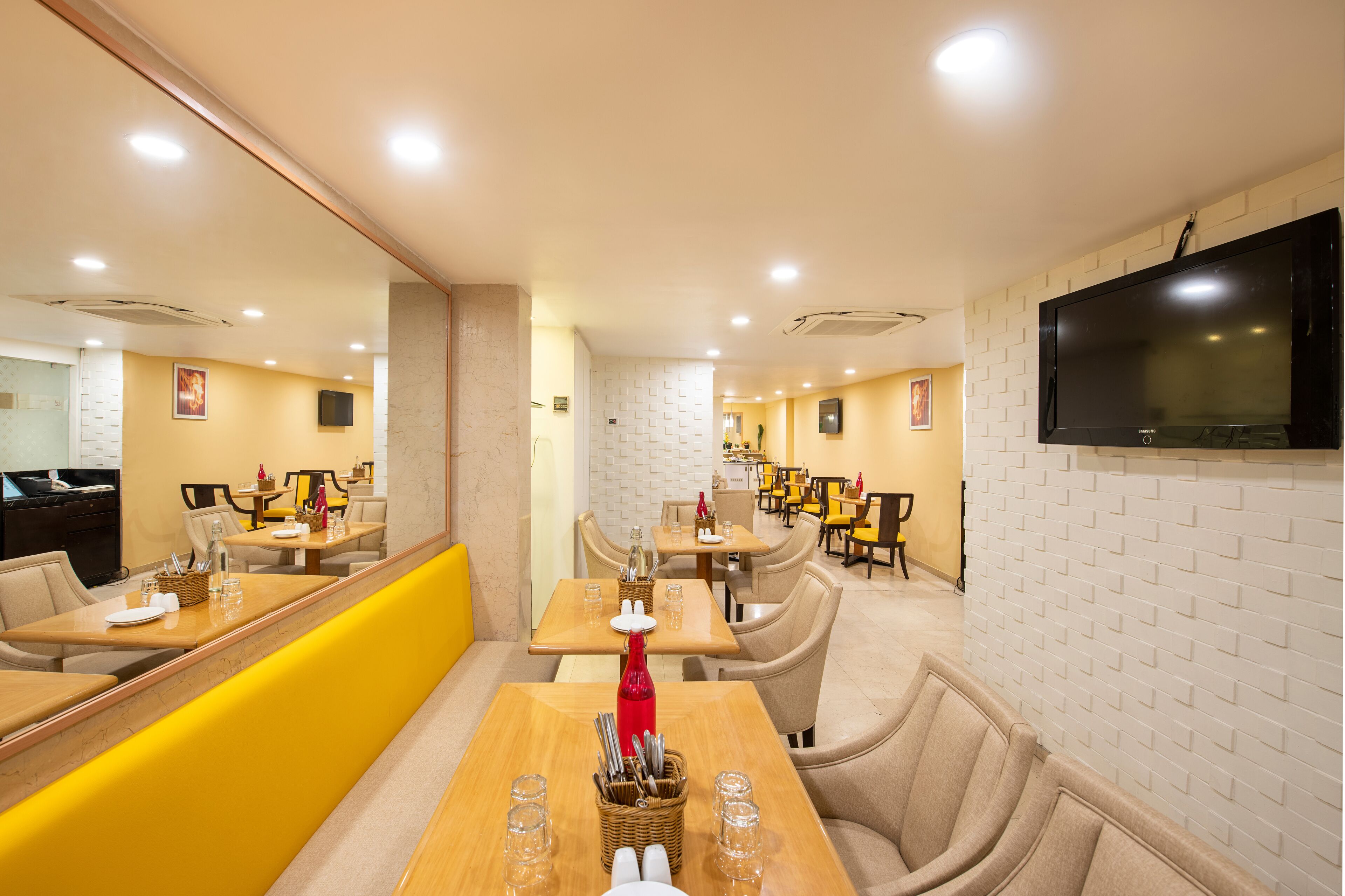 A restaurant with multiple tables and booths, a TV mounted on the wall, and a yellow accent wall.