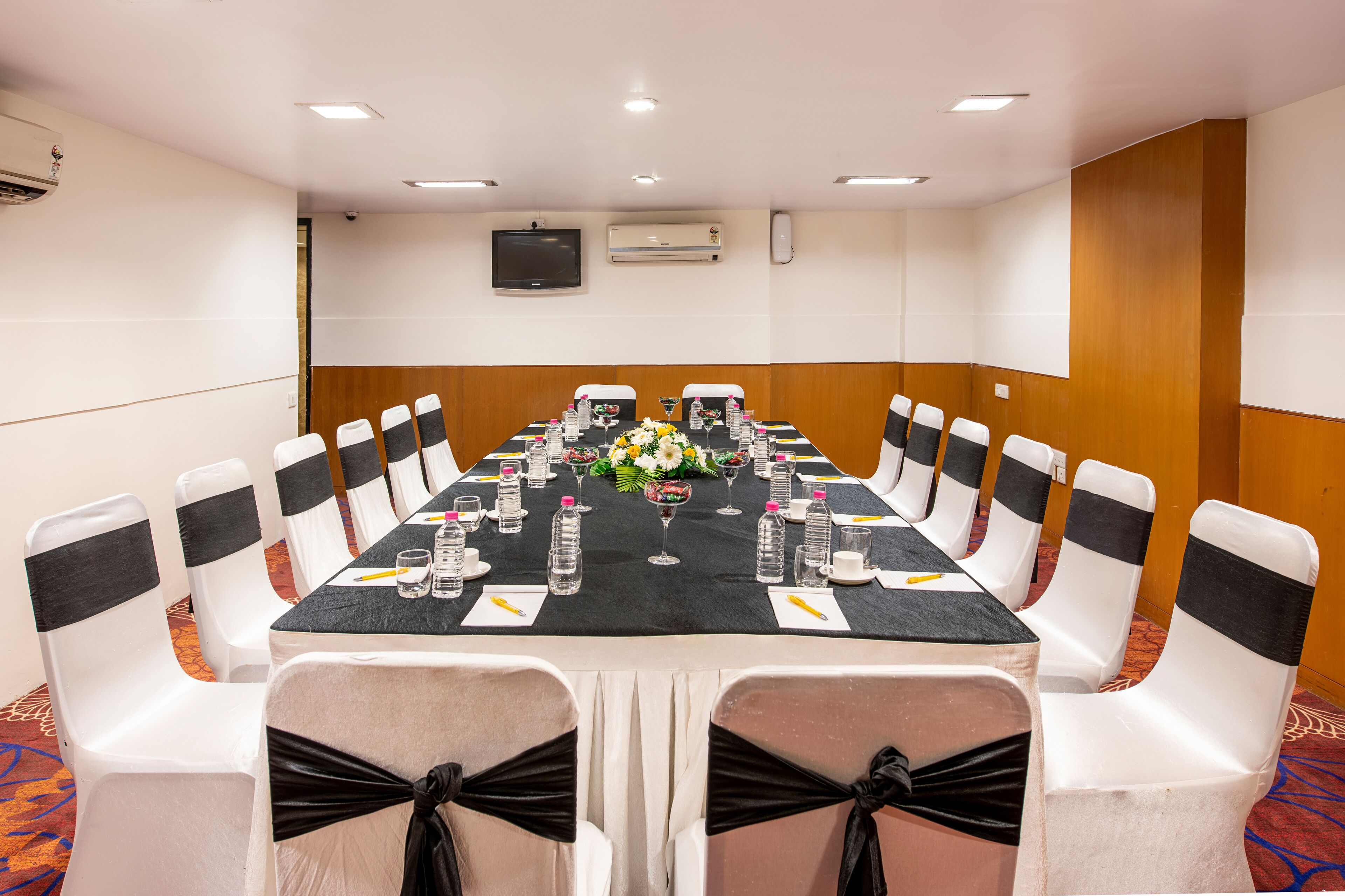 Ein Konferenzraum mit einem langen Tisch, weißen Stühlen mit schwarzen Bändern und einer schwarzen Tischdecke.