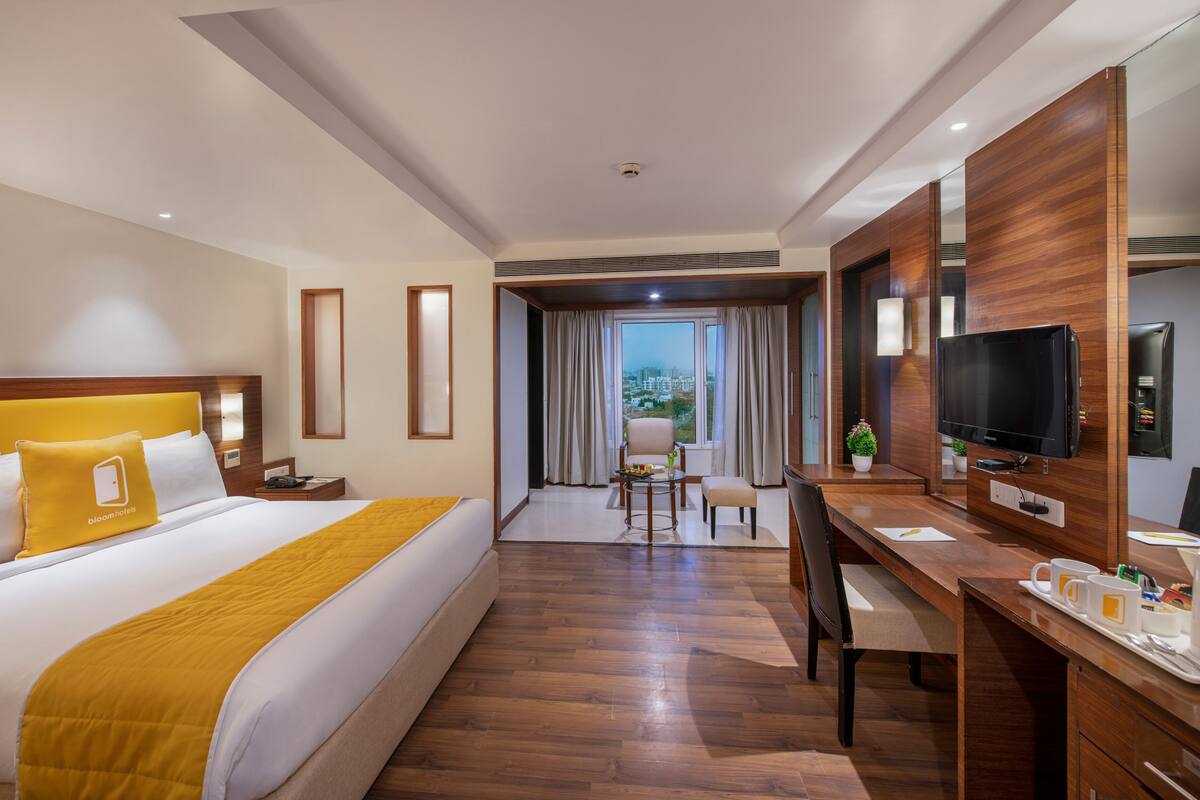 A hotel room with a large bed, a desk with a TV, a chair, and a view of the city through the window.