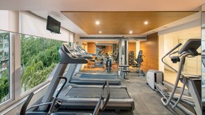 A modern gym with treadmills, weight machines, and a large window offering a view of greenery. - BloomSuites | Ahmedabad (Ahmedabad)
